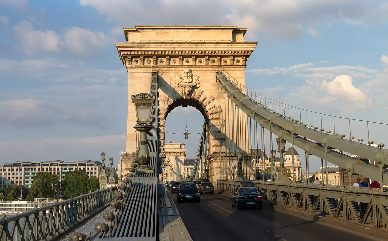 The stone gateway and suspension chains of the Széchenyi Chain Bridge with traffic crossing toward Pest