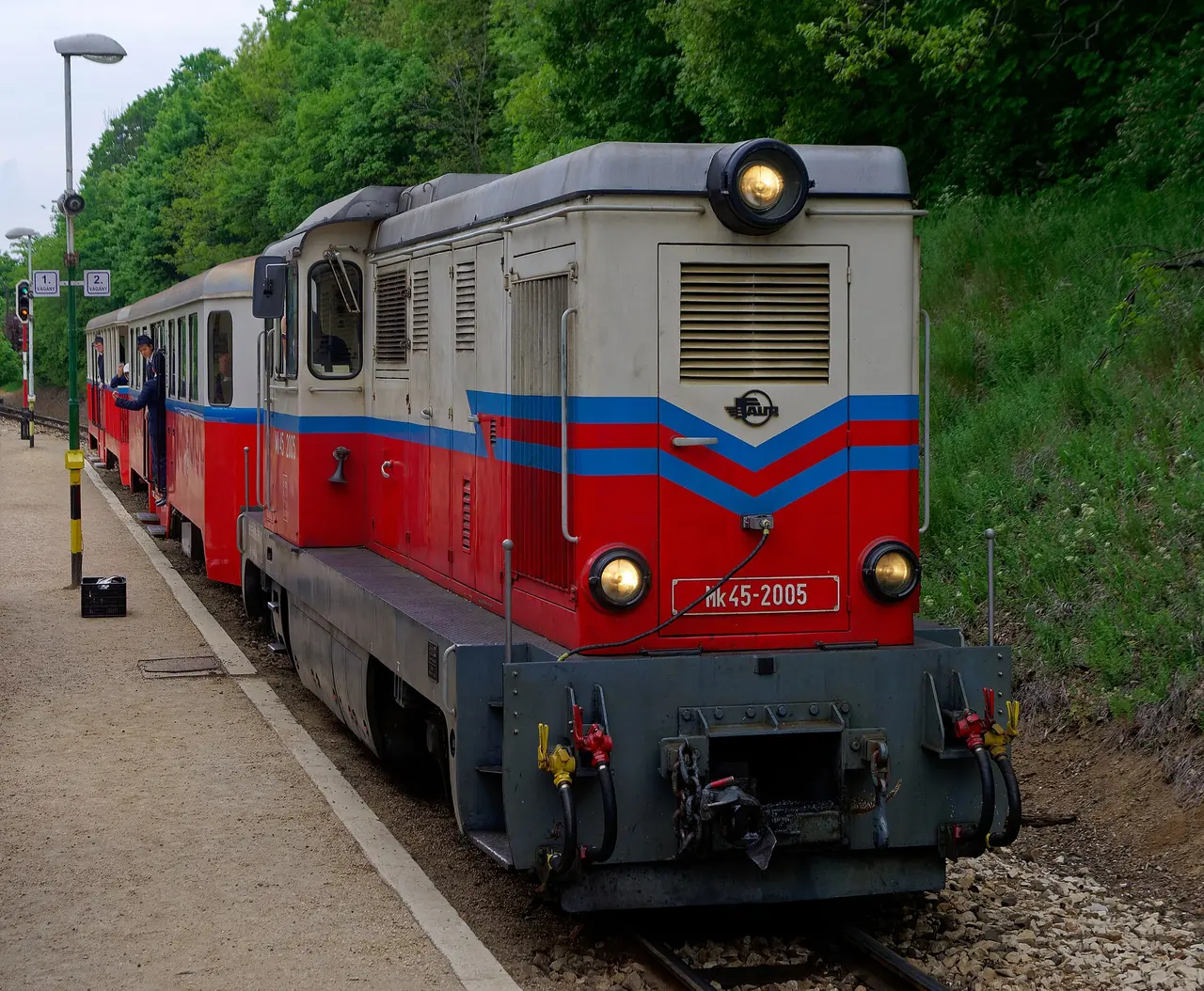 A red, blue and silver Children's Railway train standing at a platform among trees