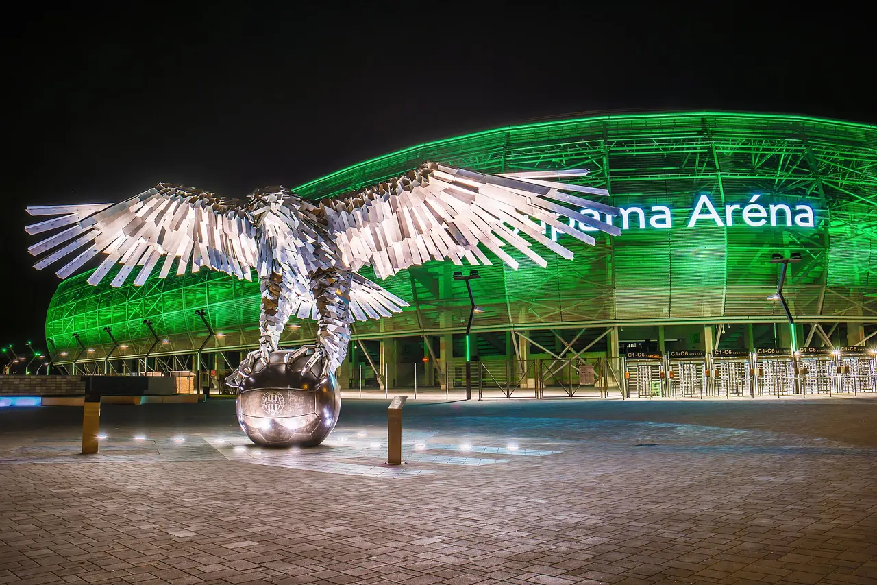 The Groupama Aréna stadium lit green at night with the bronze eagle sculpture in front, home of the Fradi Museum