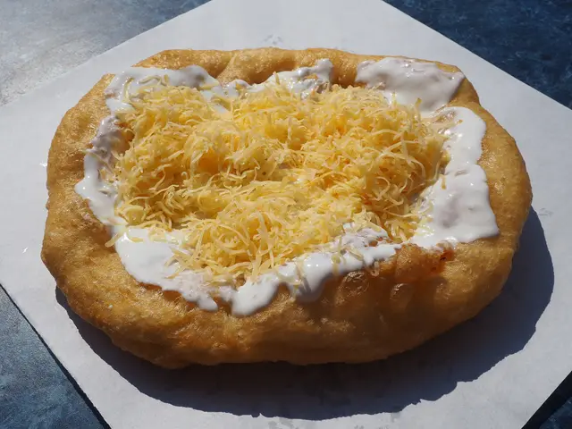 A freshly fried lángos topped with sour cream and grated cheese