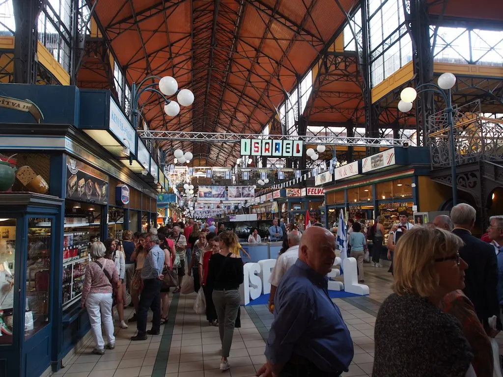 Shoppers walking between stalls under the iron roof of the Great Market Hall