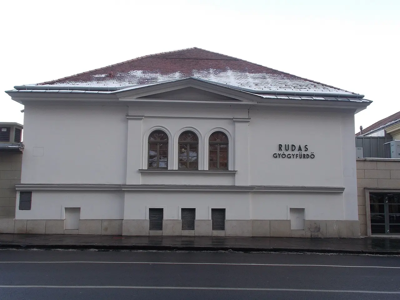 The plain white street facade of the Rudas Thermal Bath with its name above the windows