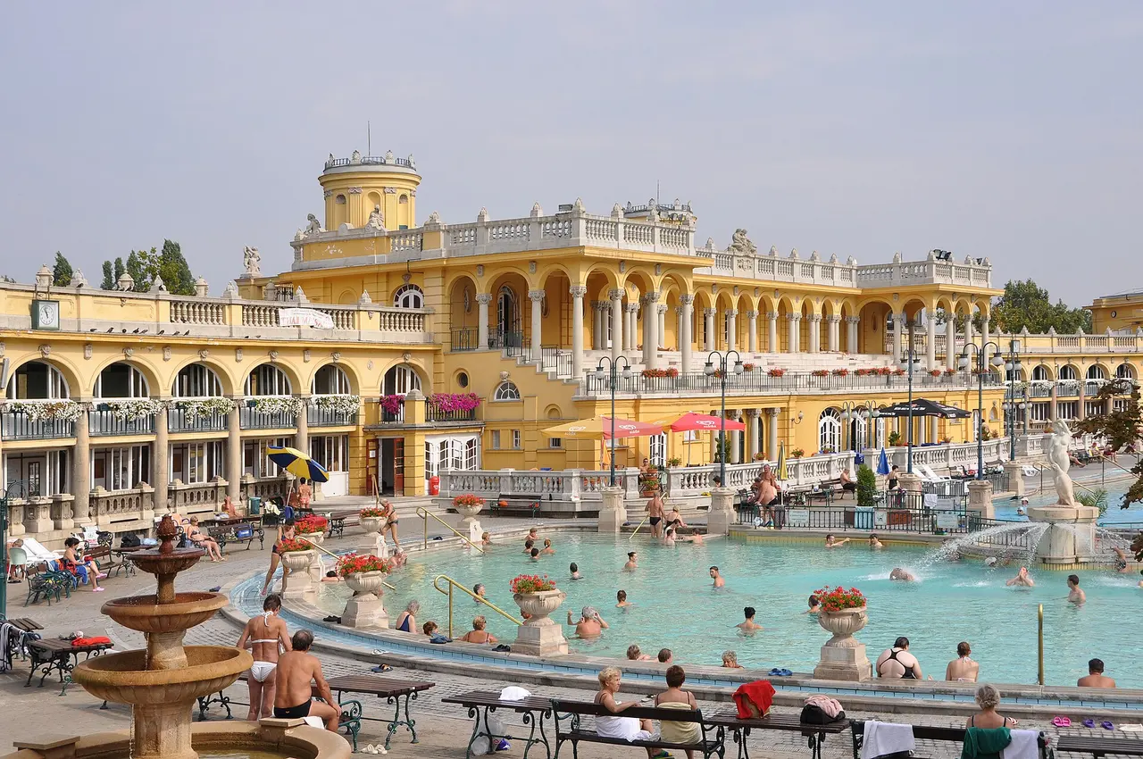 Bathers in the turquoise outdoor pool below the yellow facade of the Széchenyi Thermal Bath