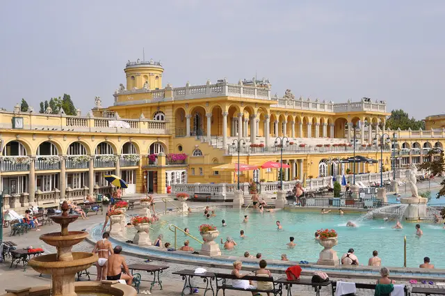 Bathers in the turquoise outdoor pool below the yellow facade of the Széchenyi Thermal Bath