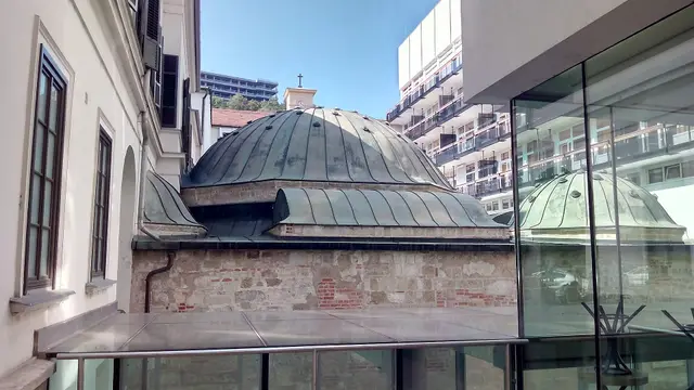 The Ottoman-era copper domes of the Veli Bej Bath beside a modern glass extension